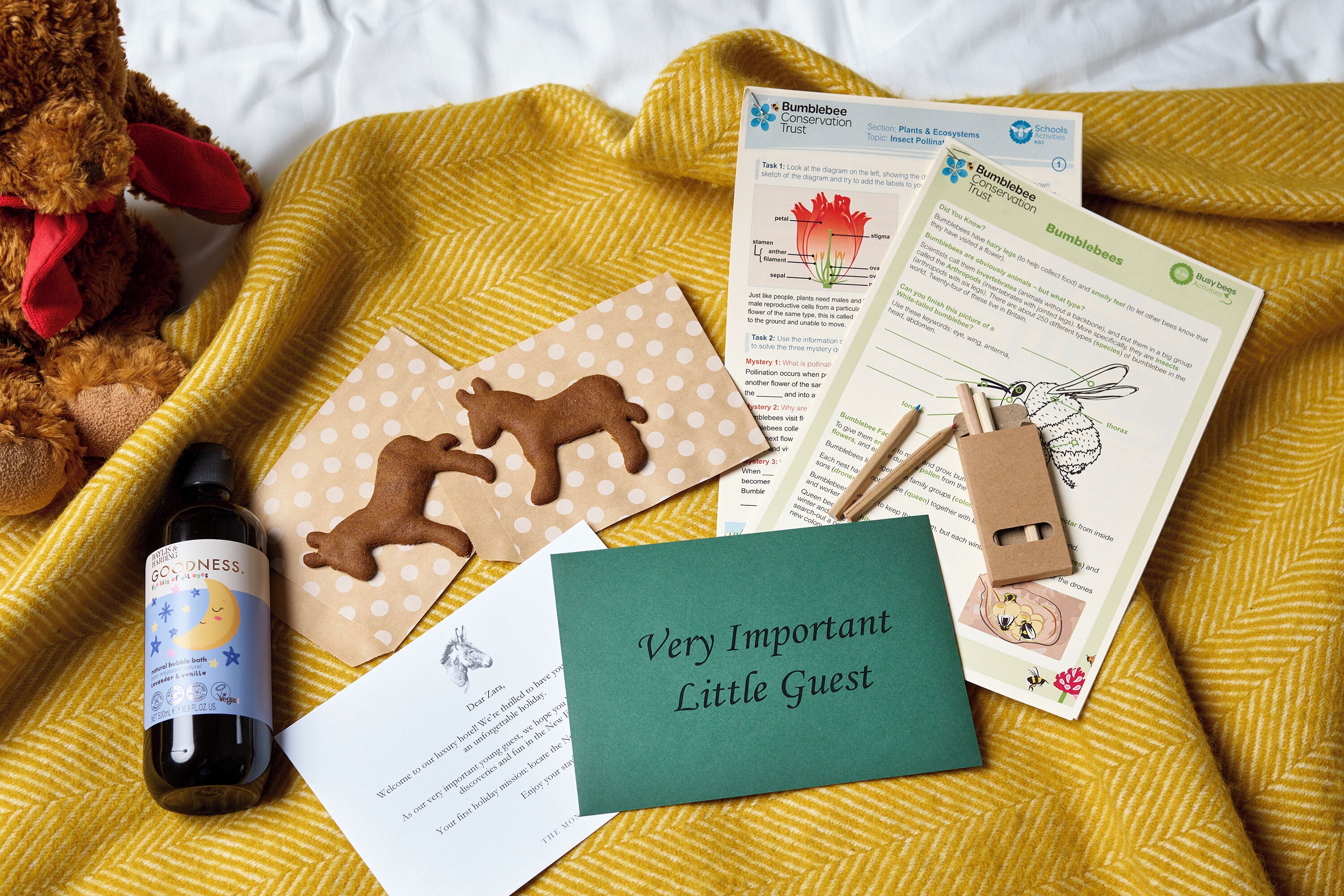 A bed with a yellow blanket, a teddy bear, a bottle, and educational materials about bees.