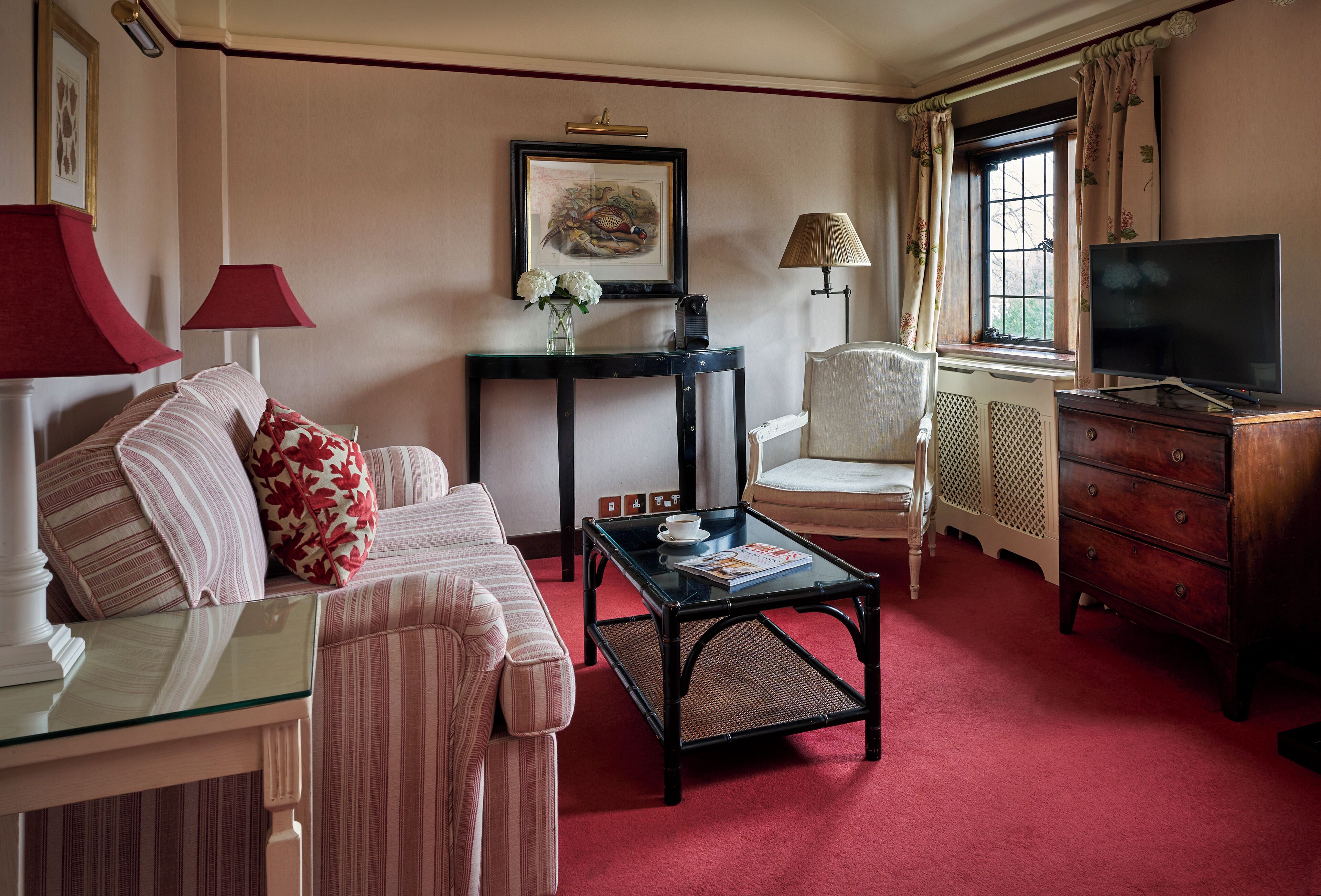 A well-appointed hotel room with a red carpet, a sofa set, a coffee table, a television, and a window with curtains.