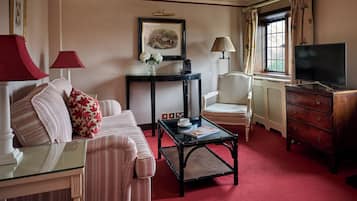 A well-appointed hotel room with a red carpet, a sofa set, a coffee table, a television, and a window with curtains.