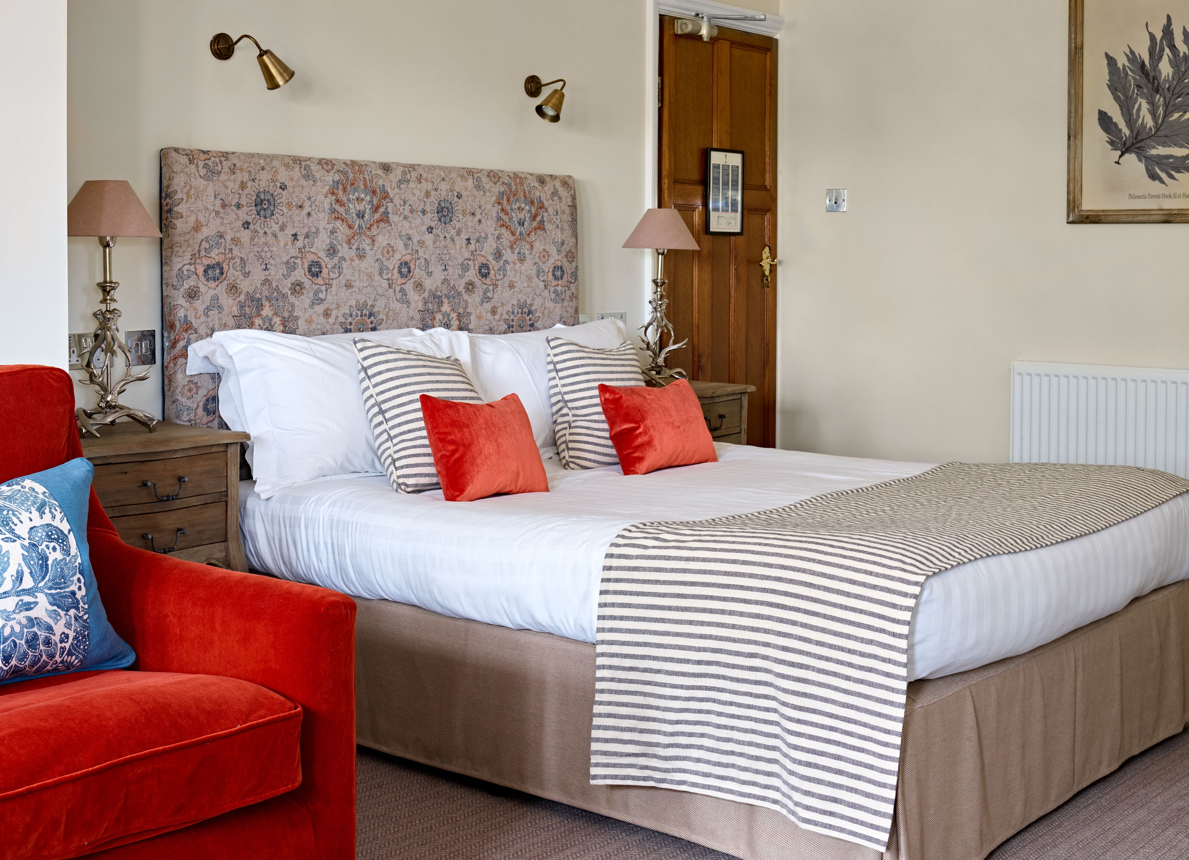 A bedroom with a large bed, striped pillows, a red chair, and a patterned headboard.