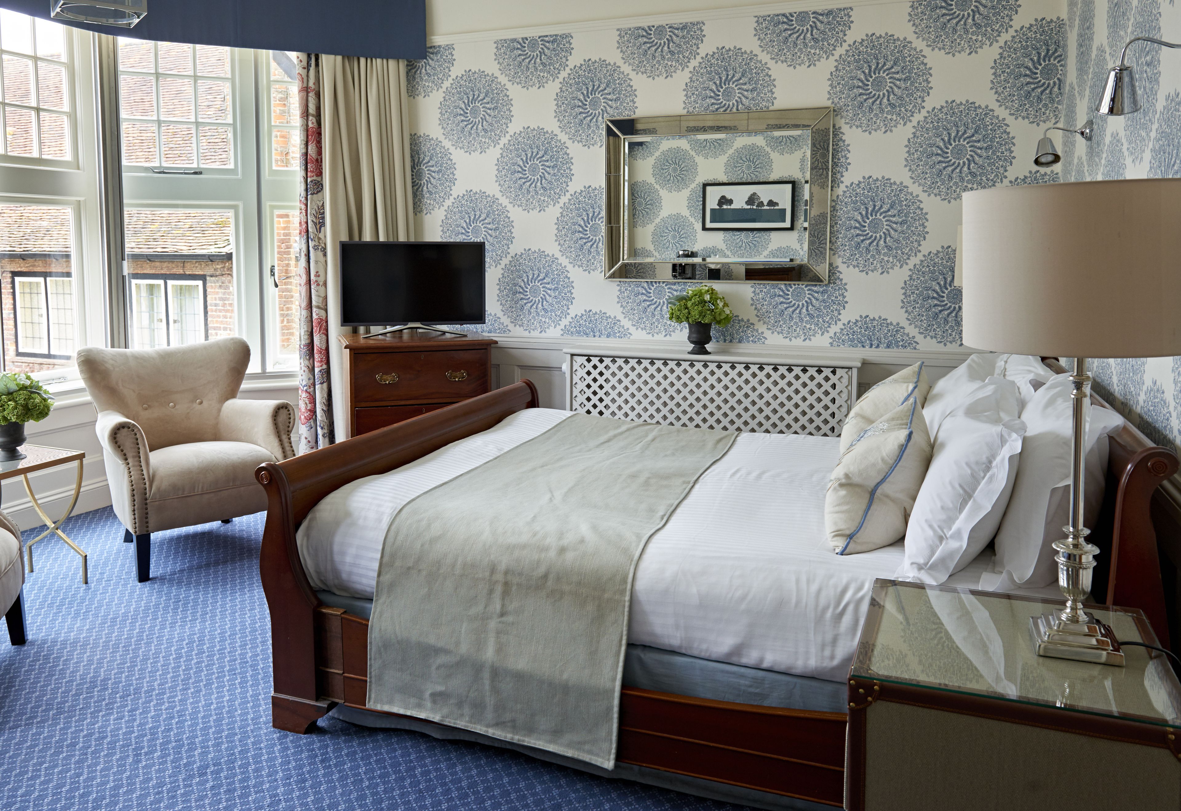 A hotel room with a large bed, a chair, a TV, a dresser, and a window with a view of a brick building.
