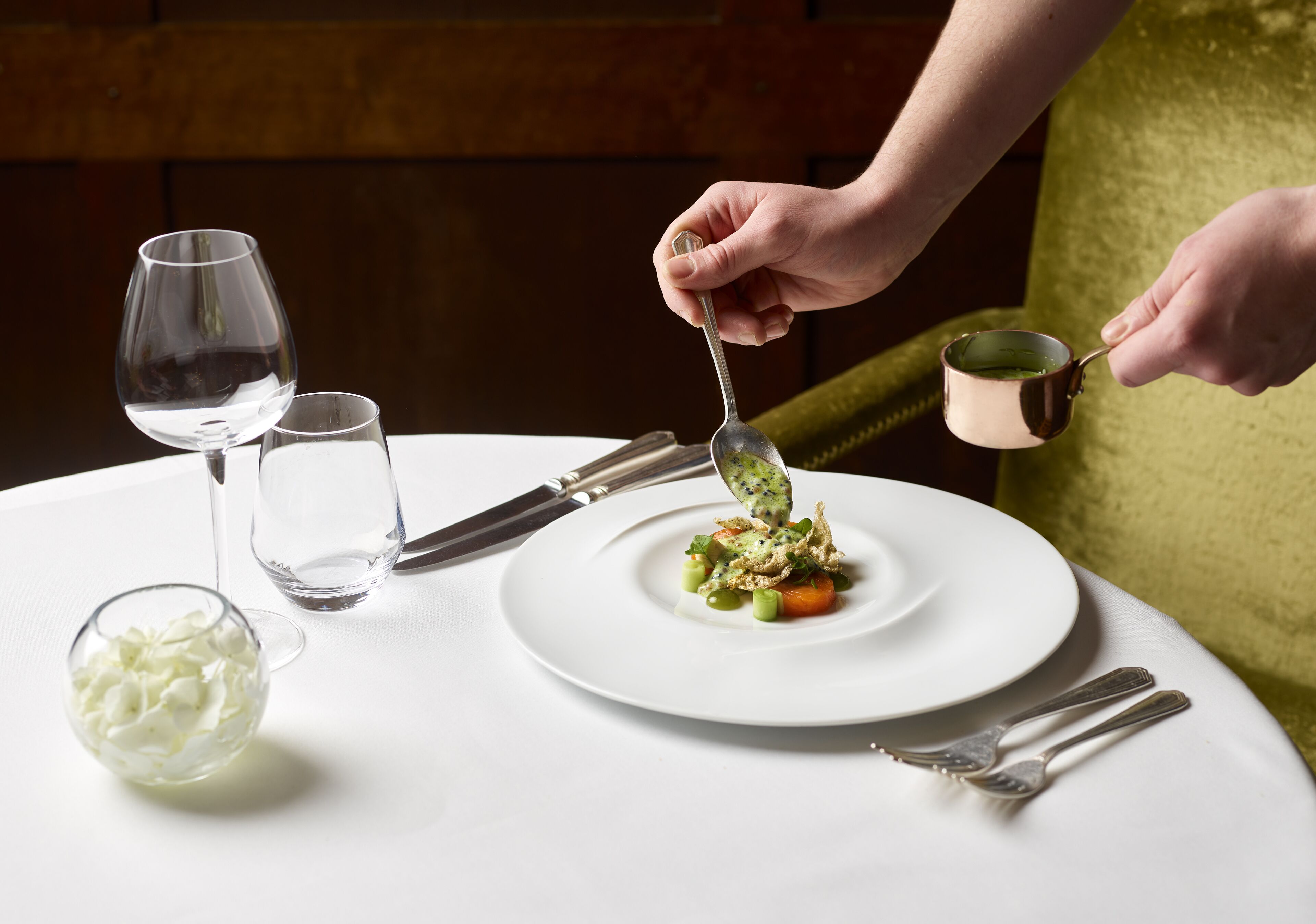 Una mesa de comedor con un plato blanco, un vaso de agua y una cuchara.