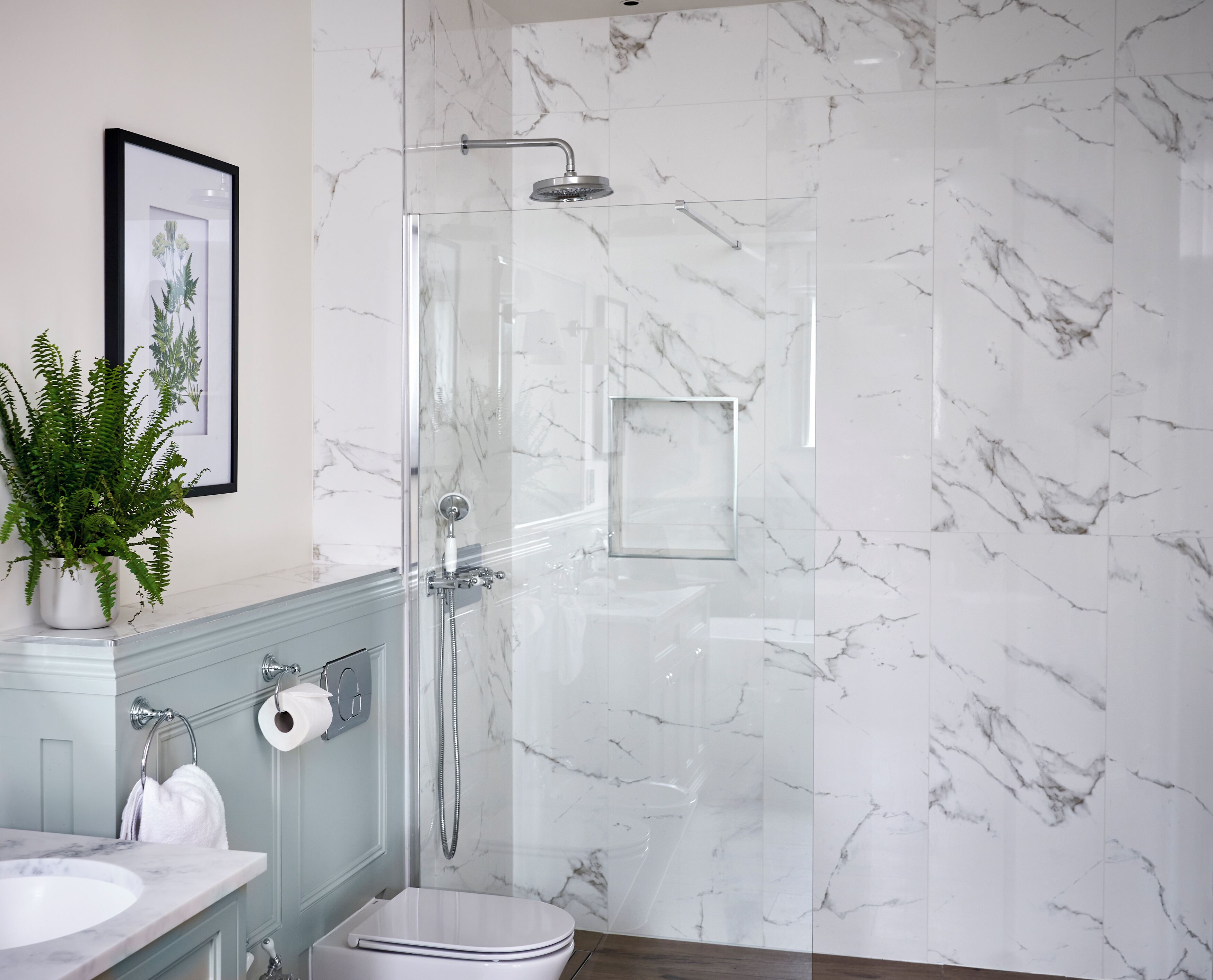 A modern bathroom with a glass-enclosed shower, marble walls, a sink, and a toilet.