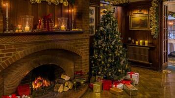 Una chimenea con un árbol de Navidad y regalos, paredes de madera y un repisa con velas y adornos.