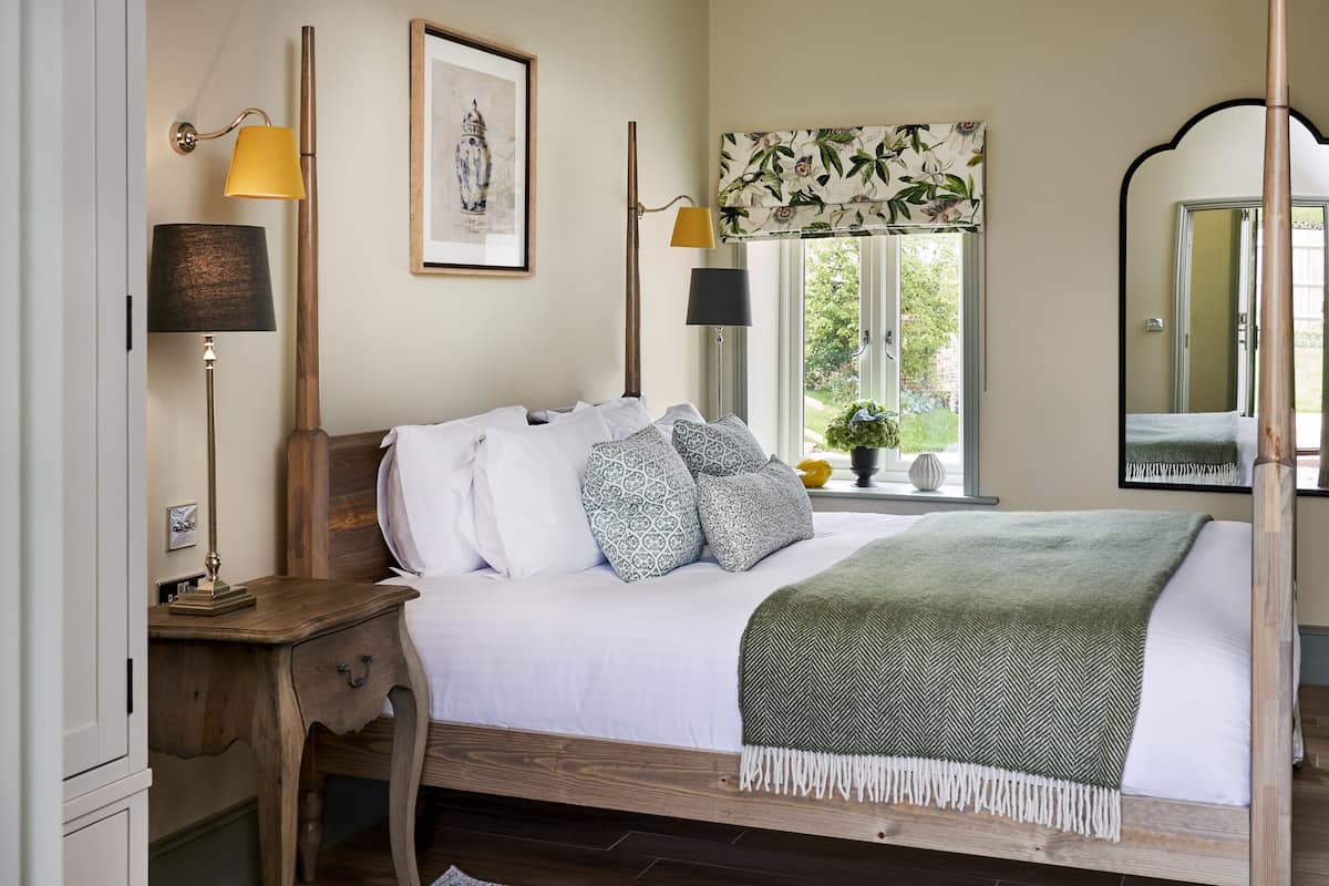 A neatly arranged bedroom with a wooden bed, two bedside lamps, a window with a view of greenery, and a mirror on the wall.