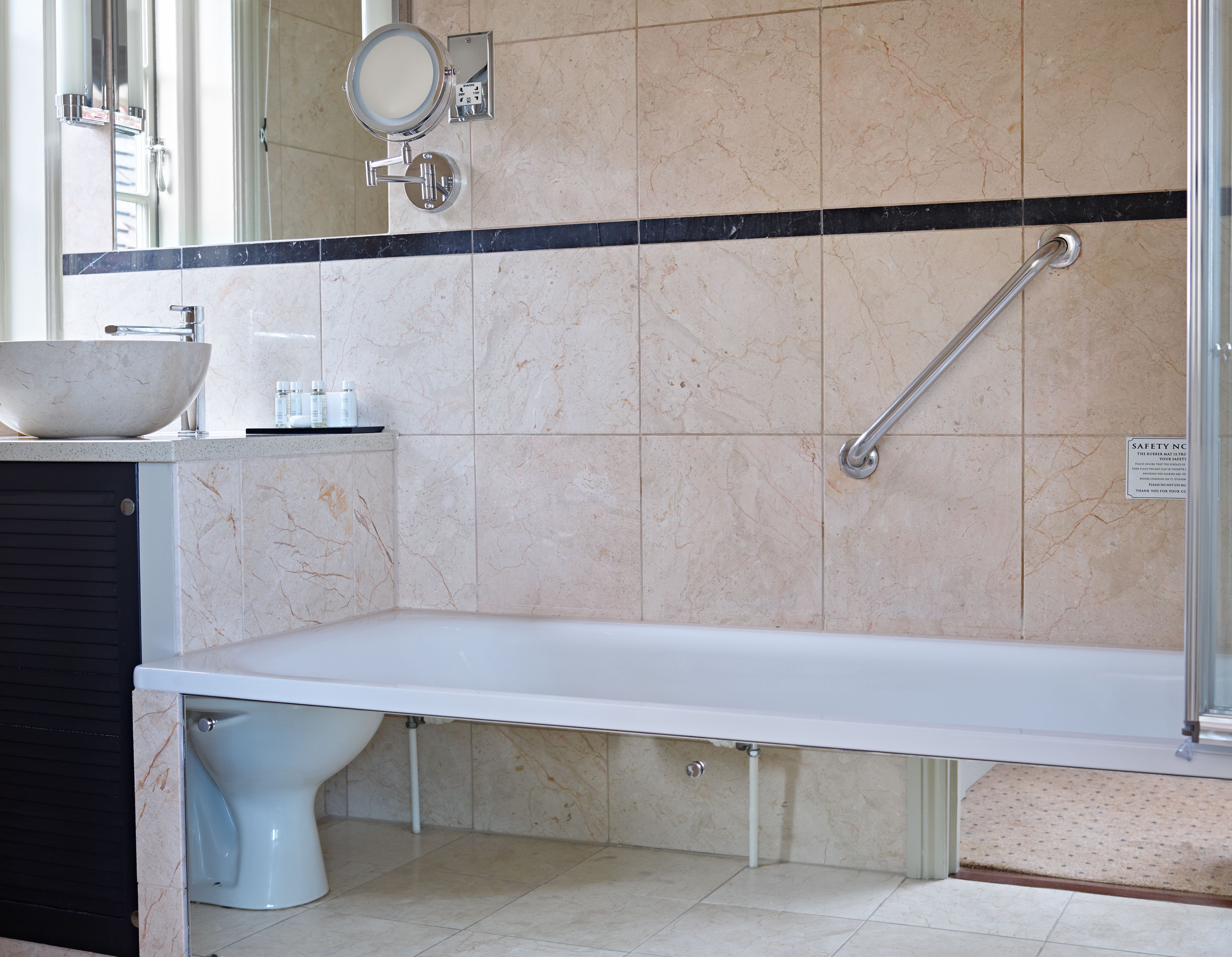 A bathroom with a large sink, a mirror, a handheld mirror, a grab bar, and a toilet.