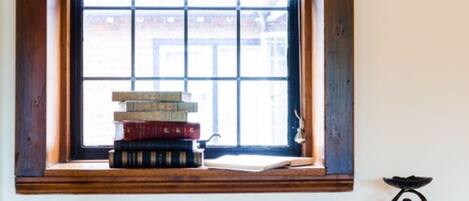 A window with a view of a building, a stack of books on a ledge, and a sculpture on the wall.