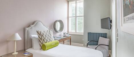 Un dormitorio ordenado con cama, mesita de noche, lámpara y una silla.