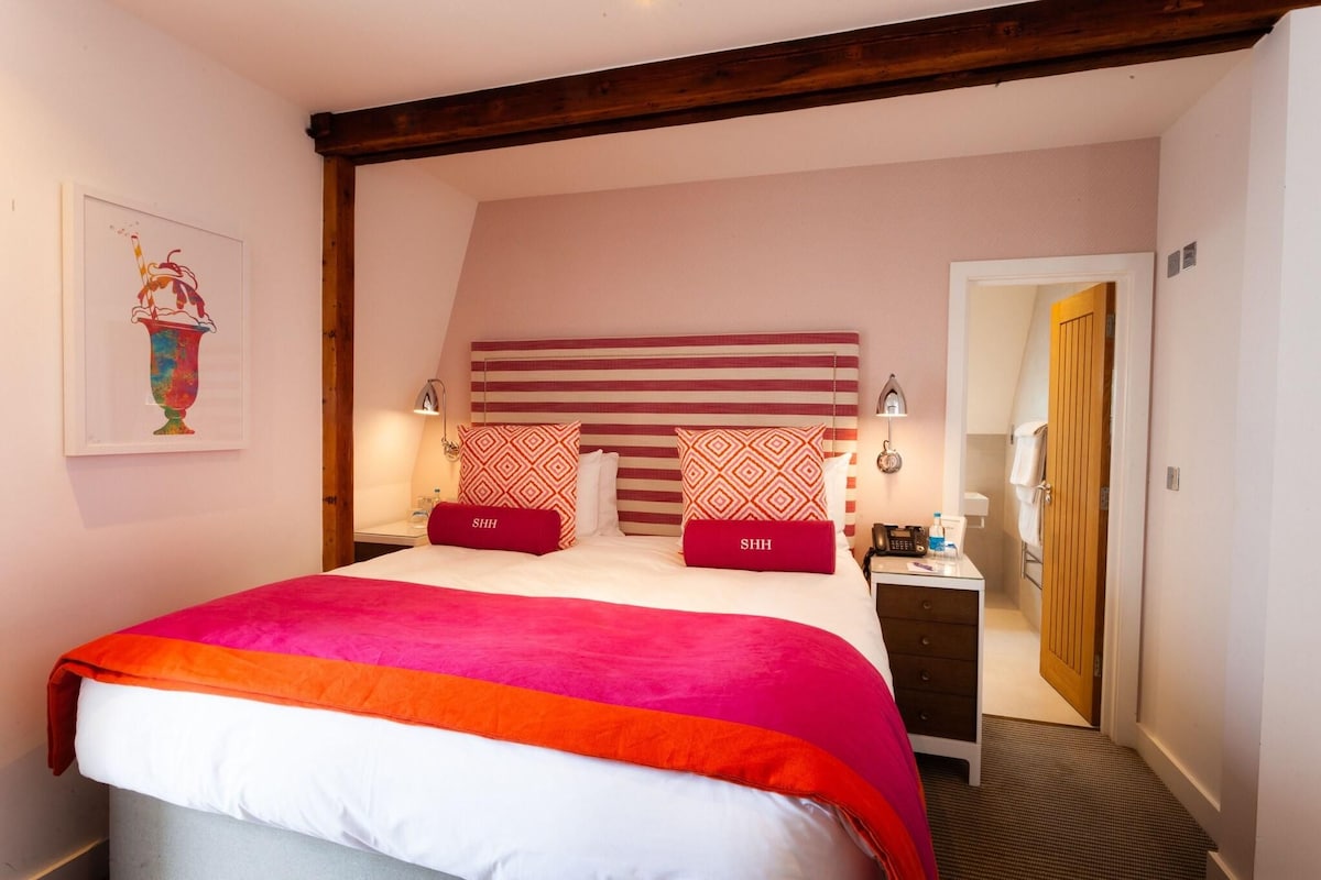 A bedroom with a large bed, two bedside tables, a wooden headboard, and a door leading to a bathroom.