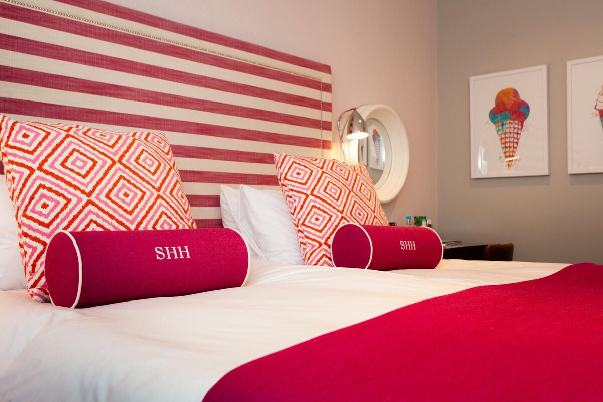 A hotel room with a striped headboard, patterned pillows, and a bed with a red blanket.