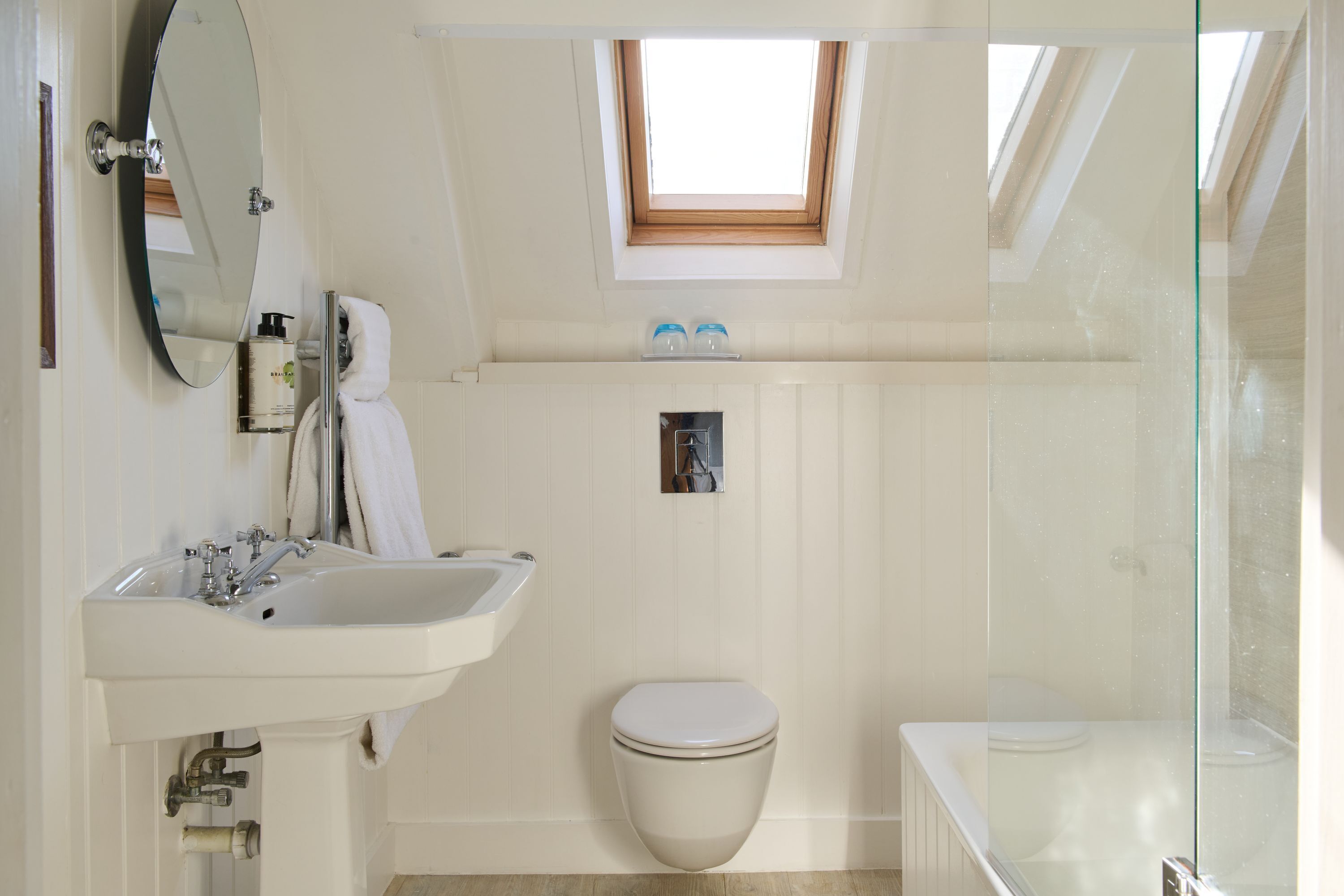 A bathroom with a skylight, a sink, a toilet, and a glass-enclosed shower area.