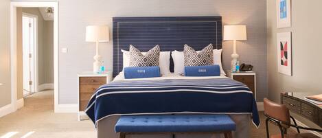A hotel room with a large bed, two bedside tables, a bench, and a desk with a chair.