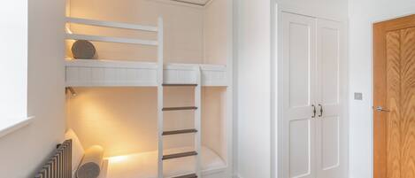 Una habitación con una cama individual superpuesta, un armario y un radiador.