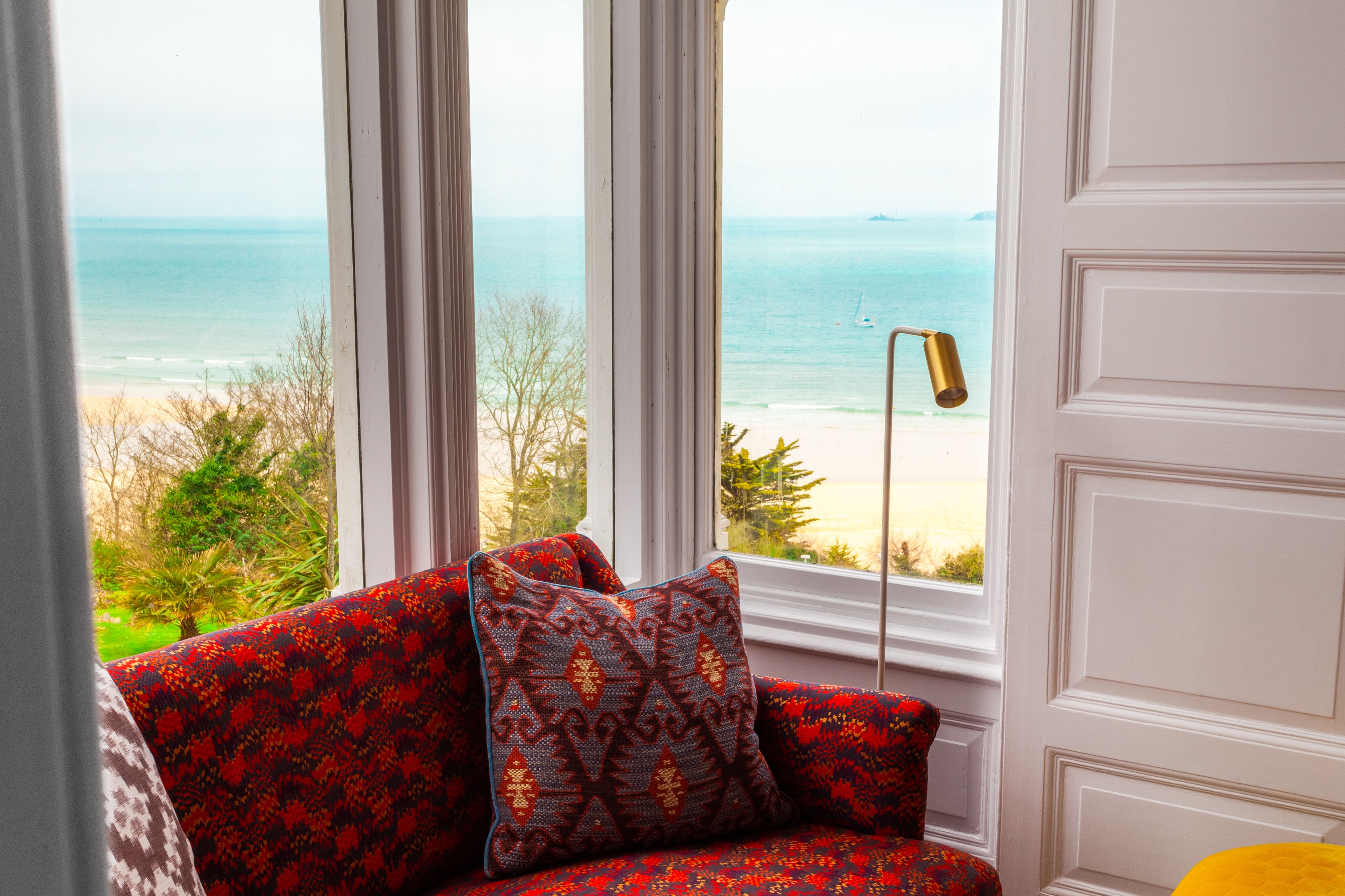 A room with a view of the beach, a patterned sofa, and a floor lamp.