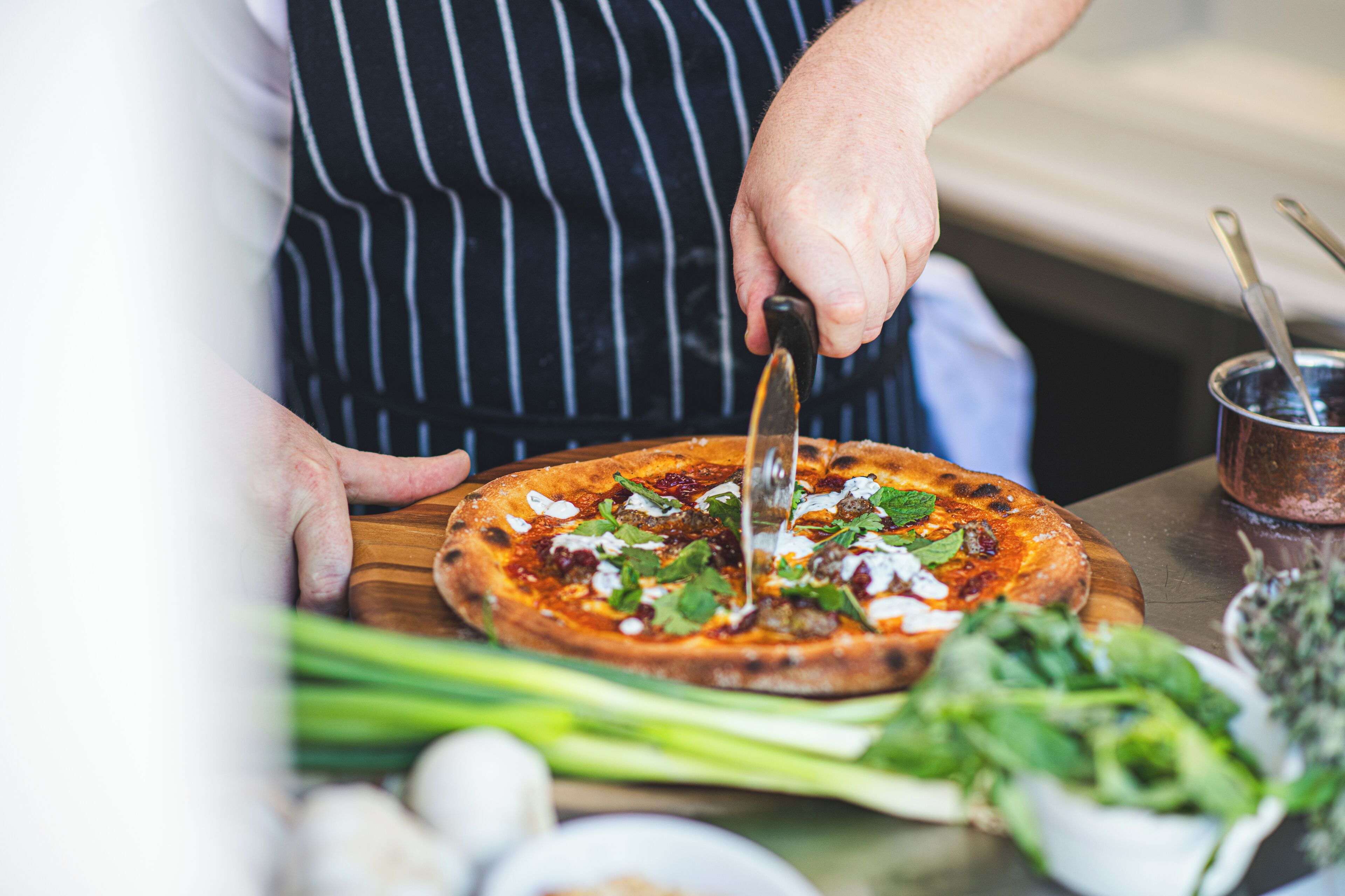 A person cutting a pizza on a wooden board.