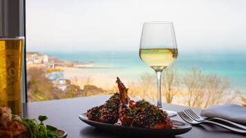 A table with a plate of food, a glass of white wine, and a view of the beach.