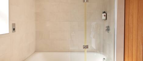 A modern bathroom with a glass-enclosed shower, a white bathtub, and a wooden door.