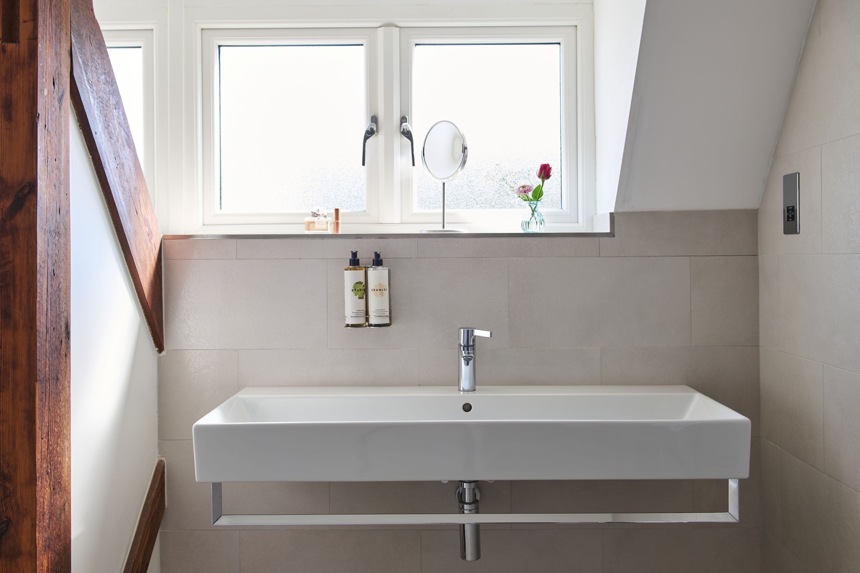 Ein modernes Badezimmer mit einem weißen Waschbecken, einem Spiegel und einem Fenster über dem Waschbecken.