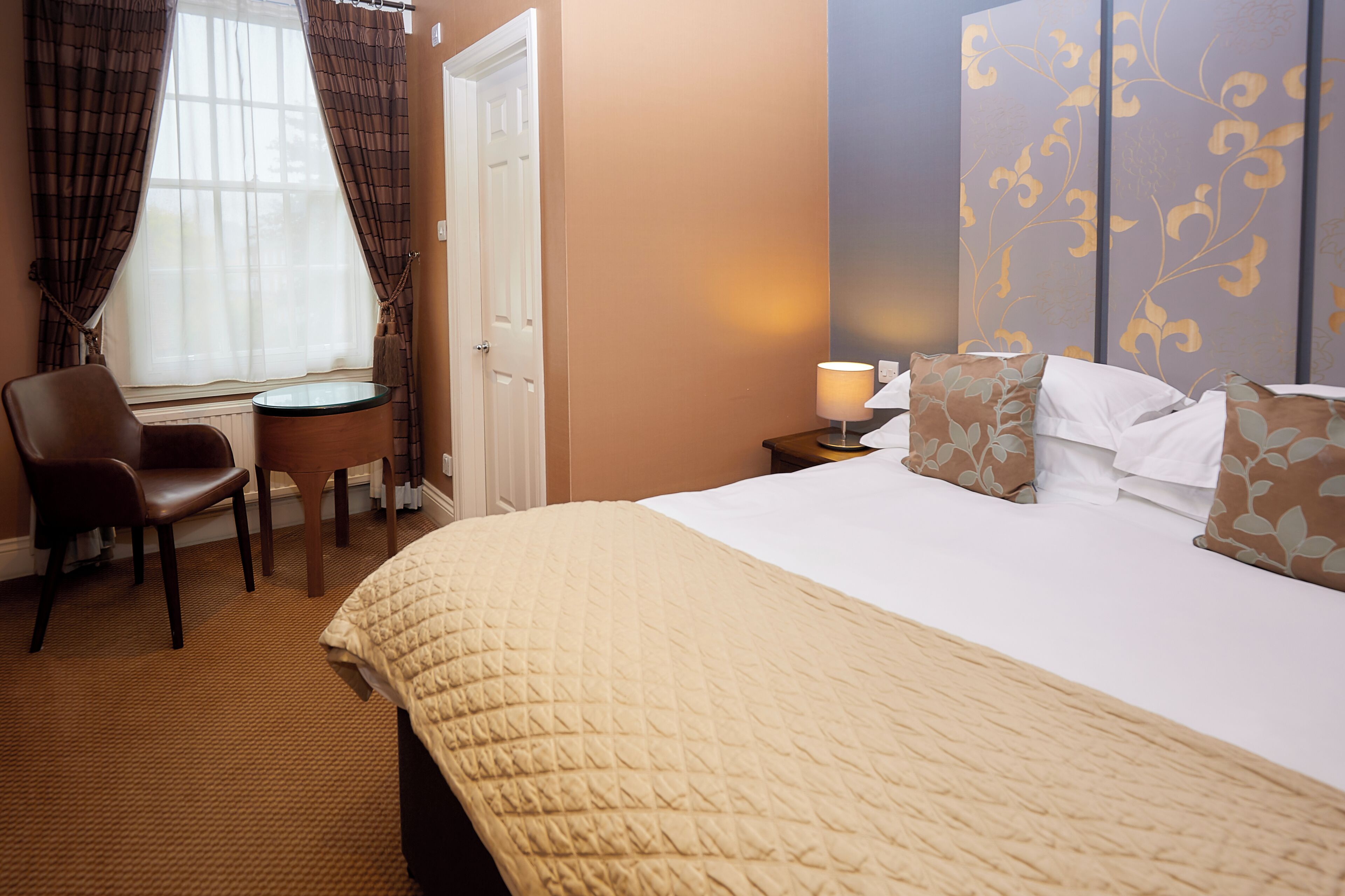 A hotel room with a bed, a chair, a small table, and a lamp.