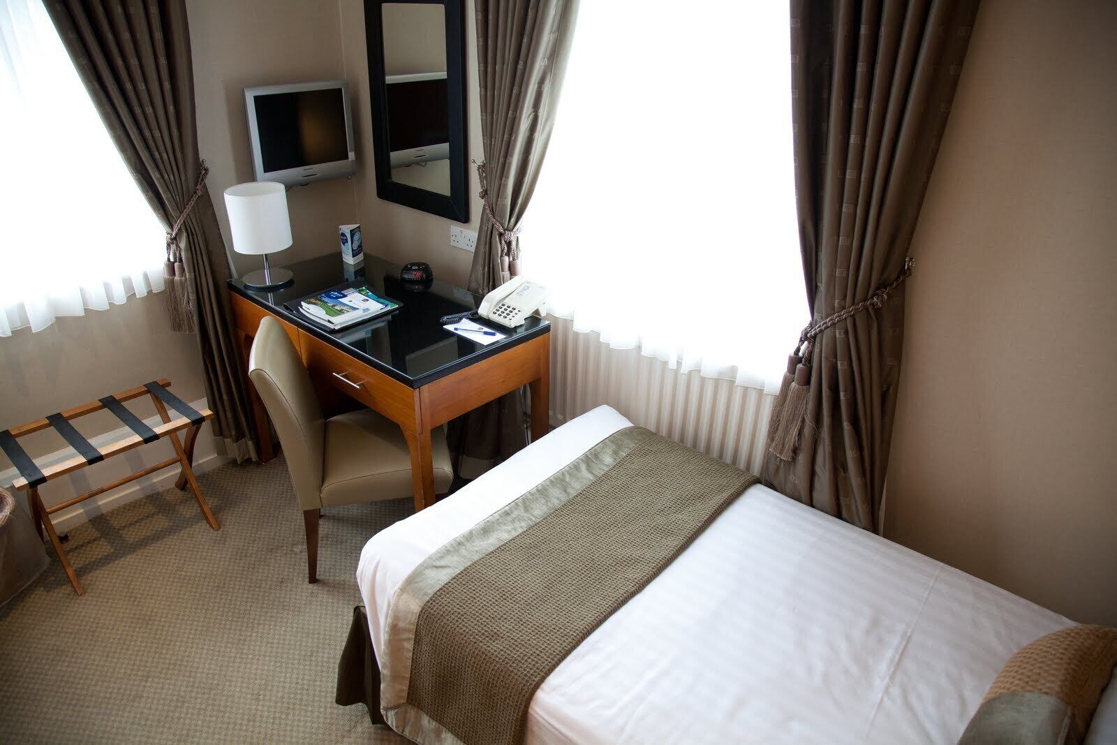 A hotel room with a bed, a desk with a chair, a telephone, and a television.