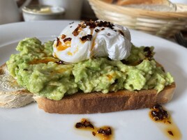 Un sándwich con crema de aguacate y un huevo pochado sobre tostada, adornado con hojuelas de chile.