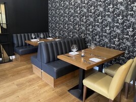 Interior de restaurante con cabinas de cuero negro, mesas de madera y un fondo de papel tapiz estampado.