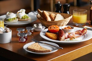 A breakfast table with toast, eggs, bacon, and a glass of orange juice.