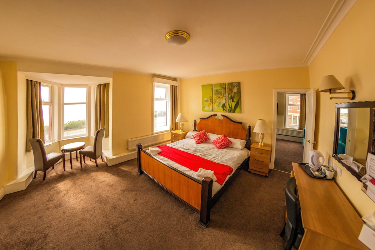 A hotel room with a large bed, two bedside tables, a desk, a chair, and a window with curtains.