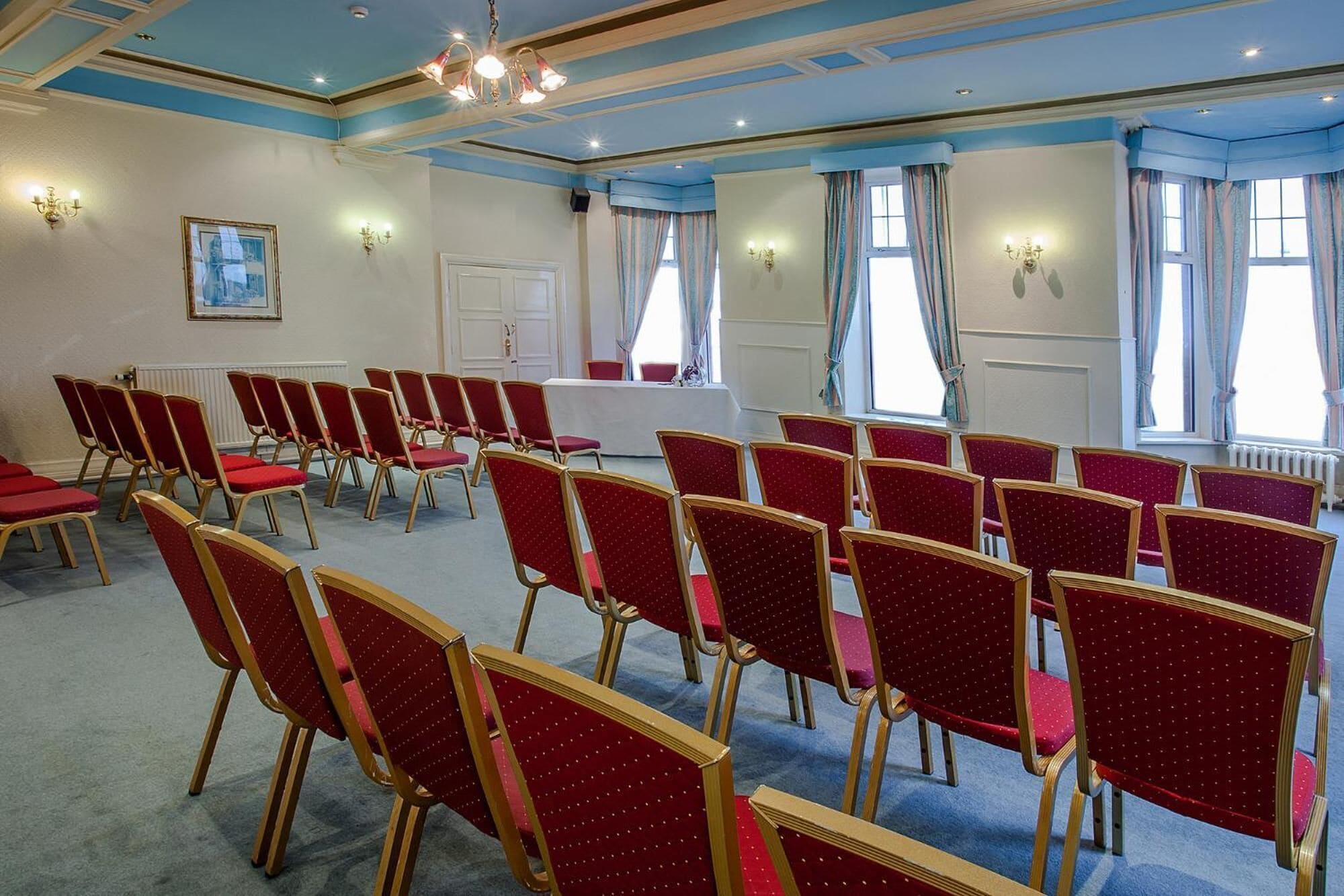 Una sala conferenze con file di sedie rosse, un tavolo bianco e un lampadario.