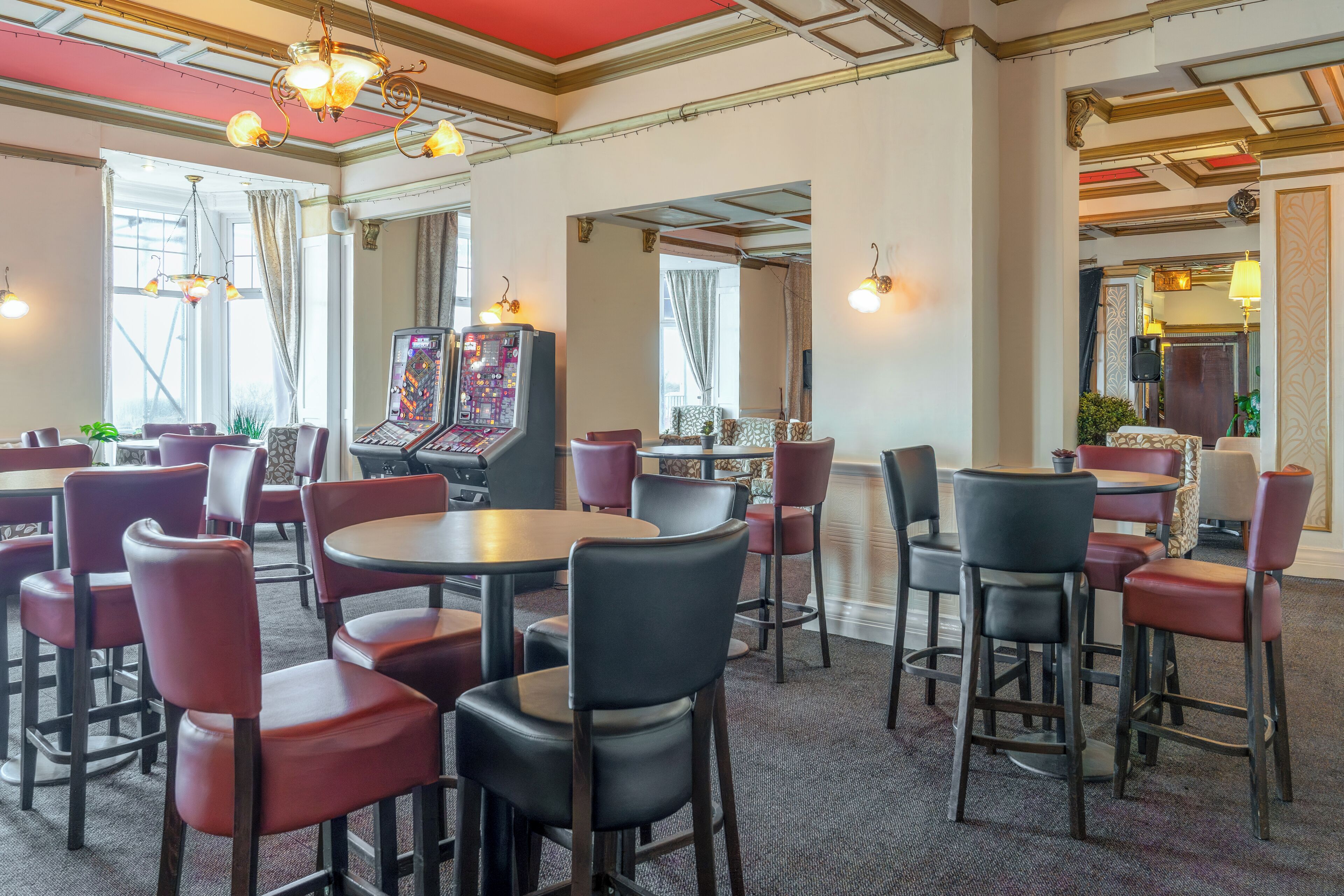 Un hall d’hôtel doté de plusieurs espaces aménagés avec des sièges, notamment des tables et des chaises, et d’un grand écran diffusant un match.