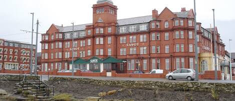 Un edificio de ladrillo rojo con el nombre 'Savoy' en la fachada, con varias ventanas y una torre central.