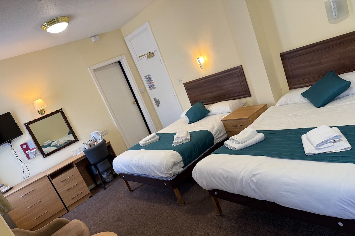 A hotel room with two beds, a desk, a chair, a mirror, and a wardrobe.