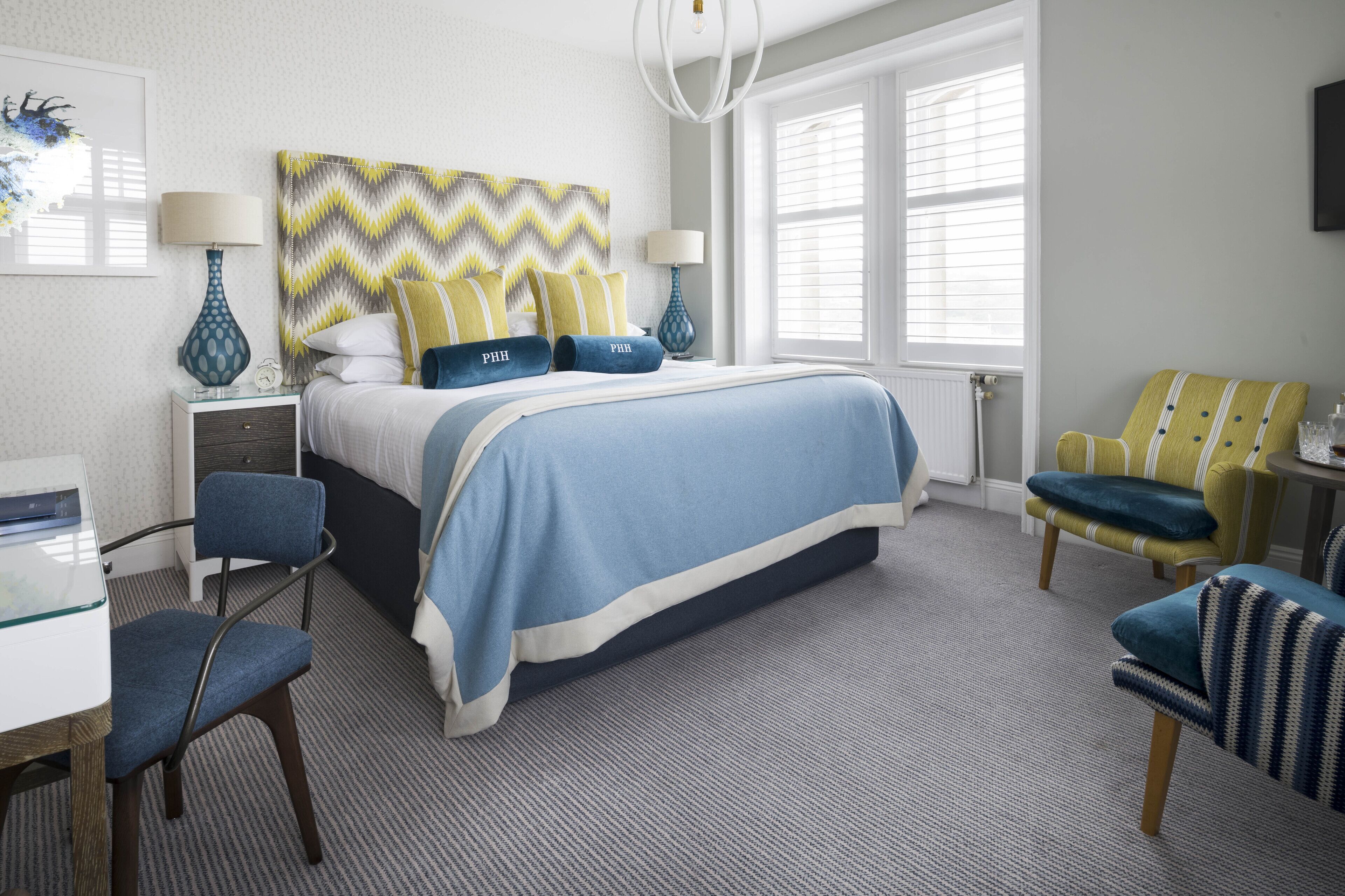 A neatly arranged hotel room with a large bed, two chairs, a desk, and a window with blinds.