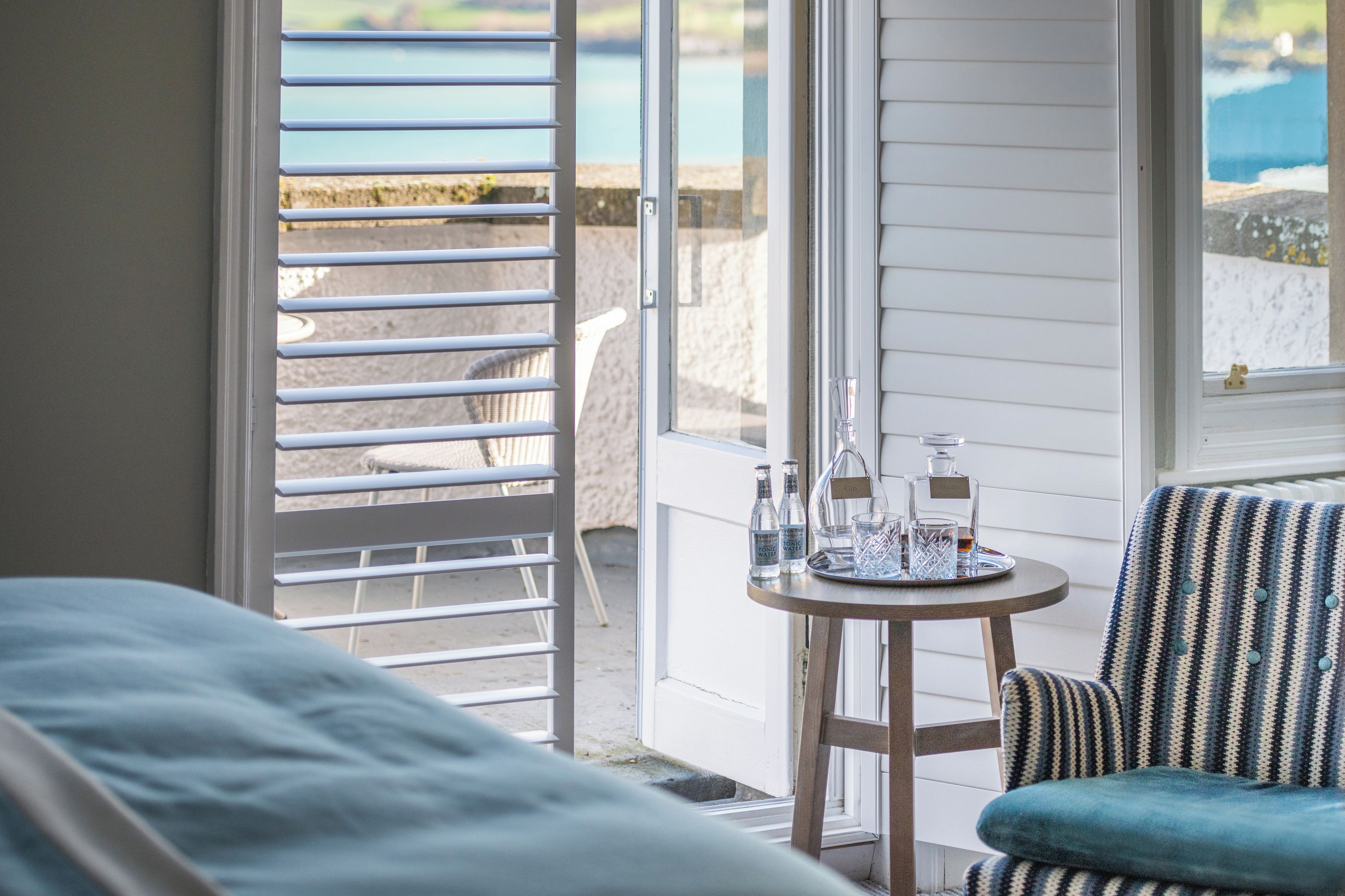 Una habitación con vista al mar, una mesa con botellas y copas, y una silla a rayas.