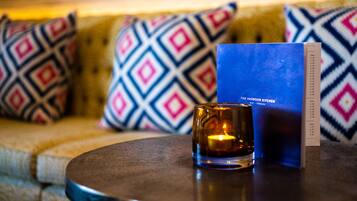 A candle on a table with a menu and a patterned cushion in the background.