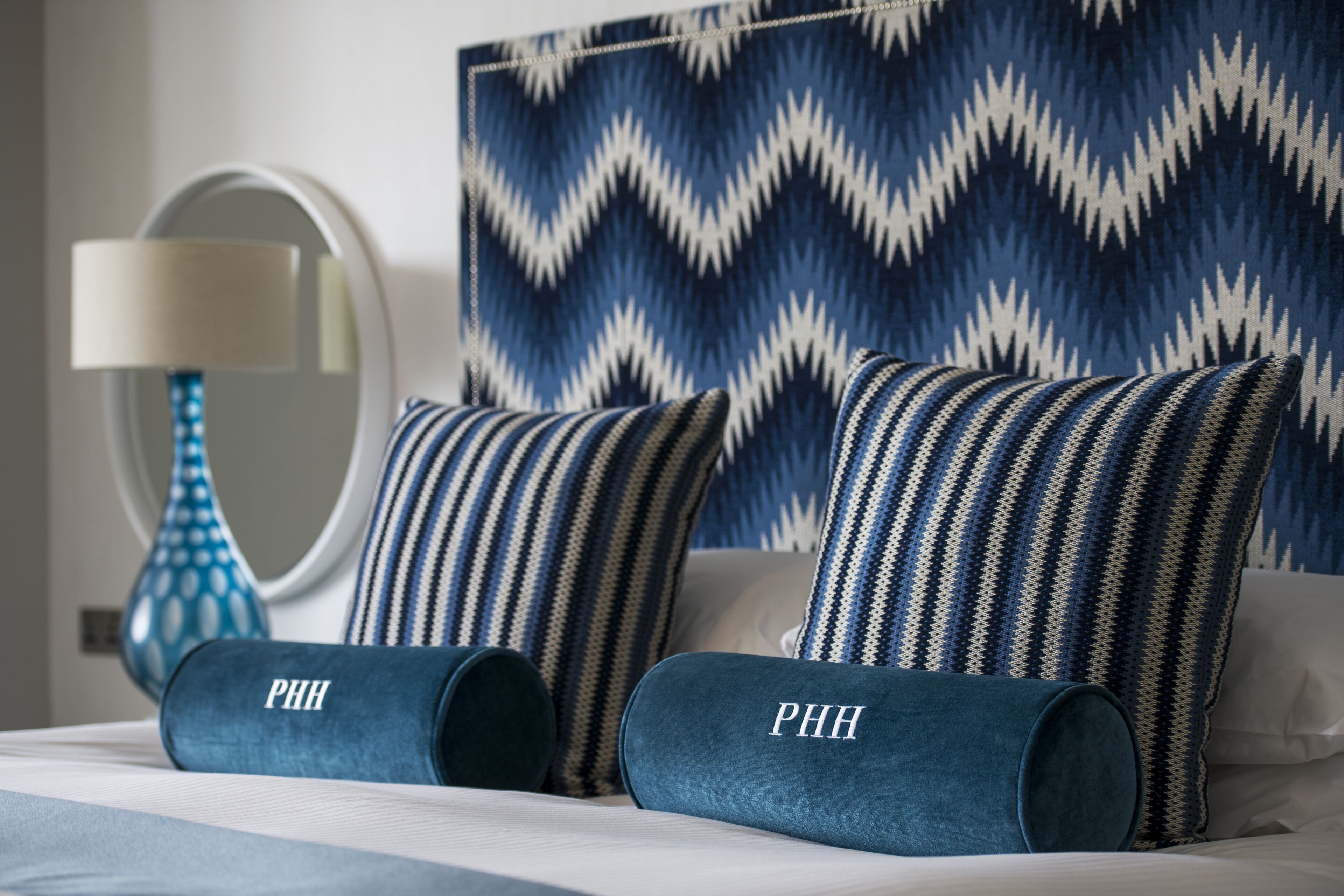 A neatly made bed with two pillows labeled "PHH" and a blue patterned wall behind it.