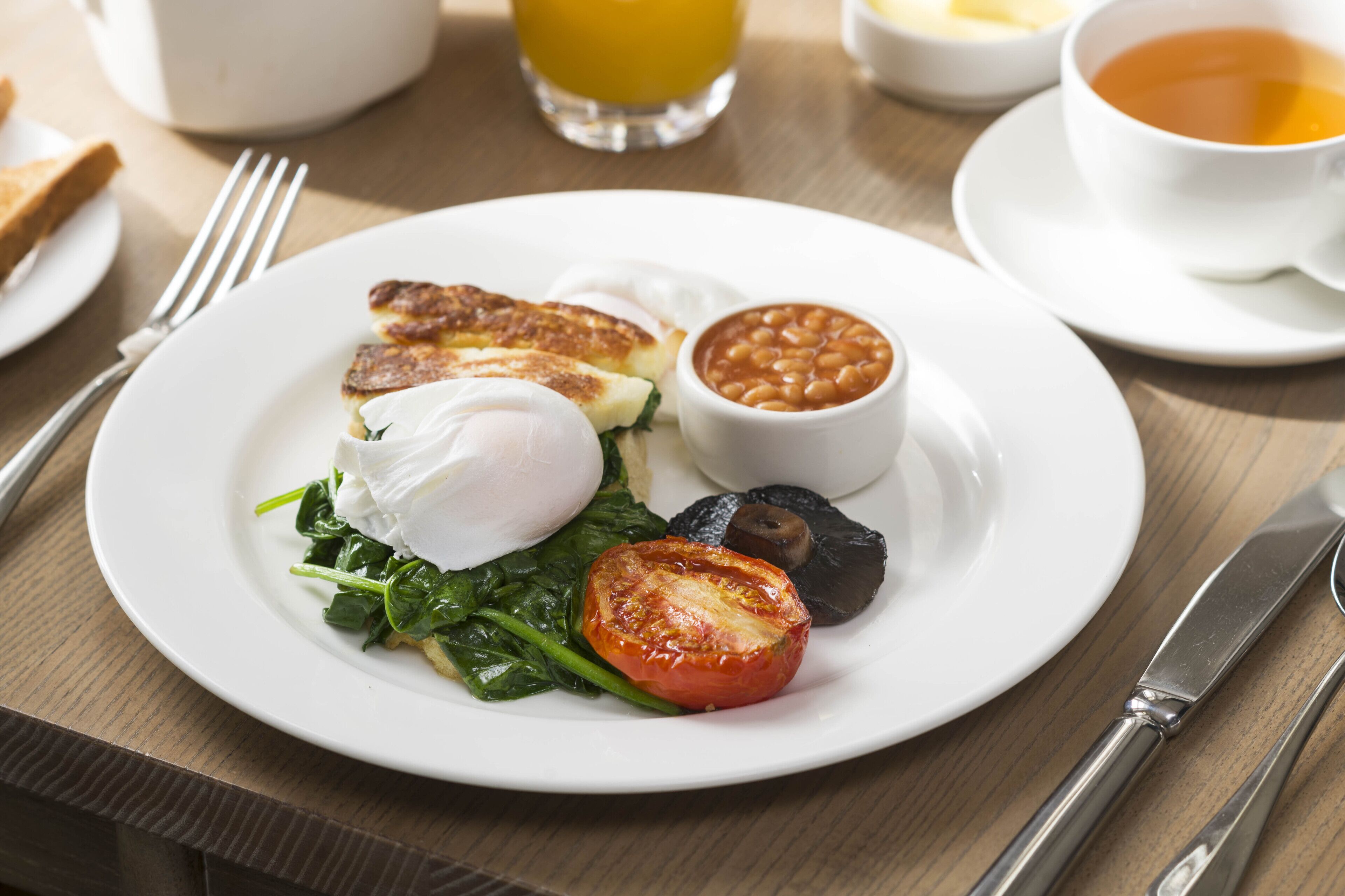A breakfast plate with eggs, beans, spinach, and tomato on a white plate.