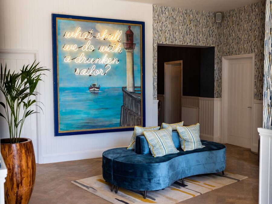 Una sala de estar con un sofá azul, un cuadro grande de un faro y una planta en maceta.
