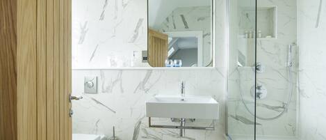 A modern bathroom with a marble backsplash, a wooden door, a white sink, a glass shower enclosure, and a mirror.