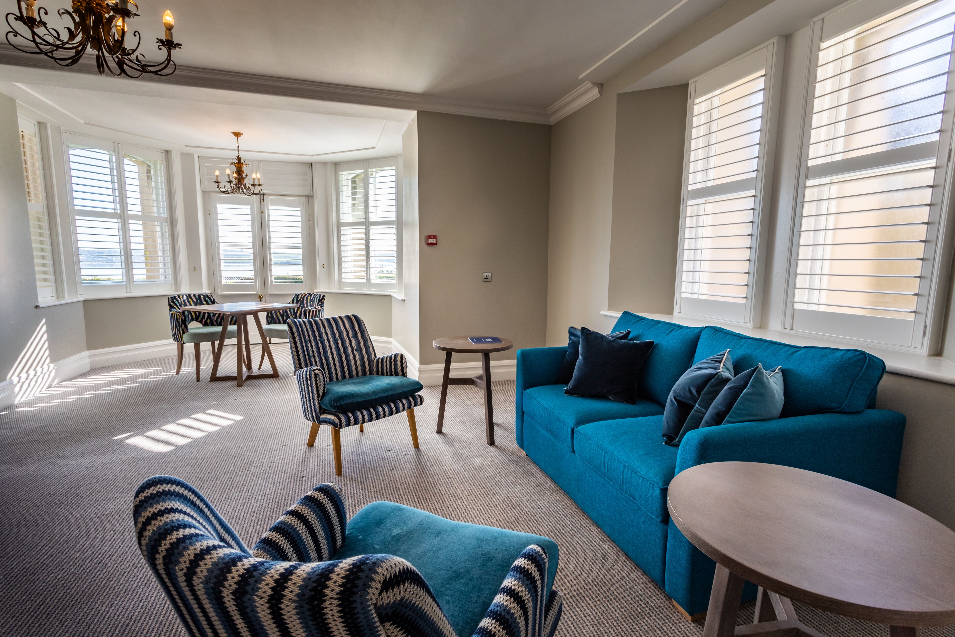 A living room with a blue sofa, striped armchairs, a round table, and a chandelier.