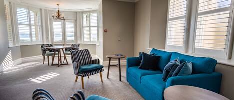 A living room with a blue sofa, striped armchairs, a round table, and a chandelier.
