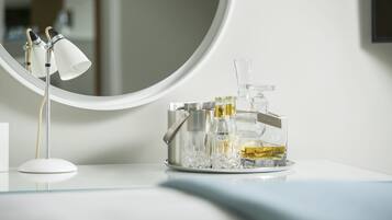 Een wastafelmeubel met een ronde spiegel, een witte lamp en een dienblad met een fles vloeistof en een glas.