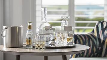 A round table with a stainless steel pitcher, a bottle of tonic water, and two glass decanters on a tray.