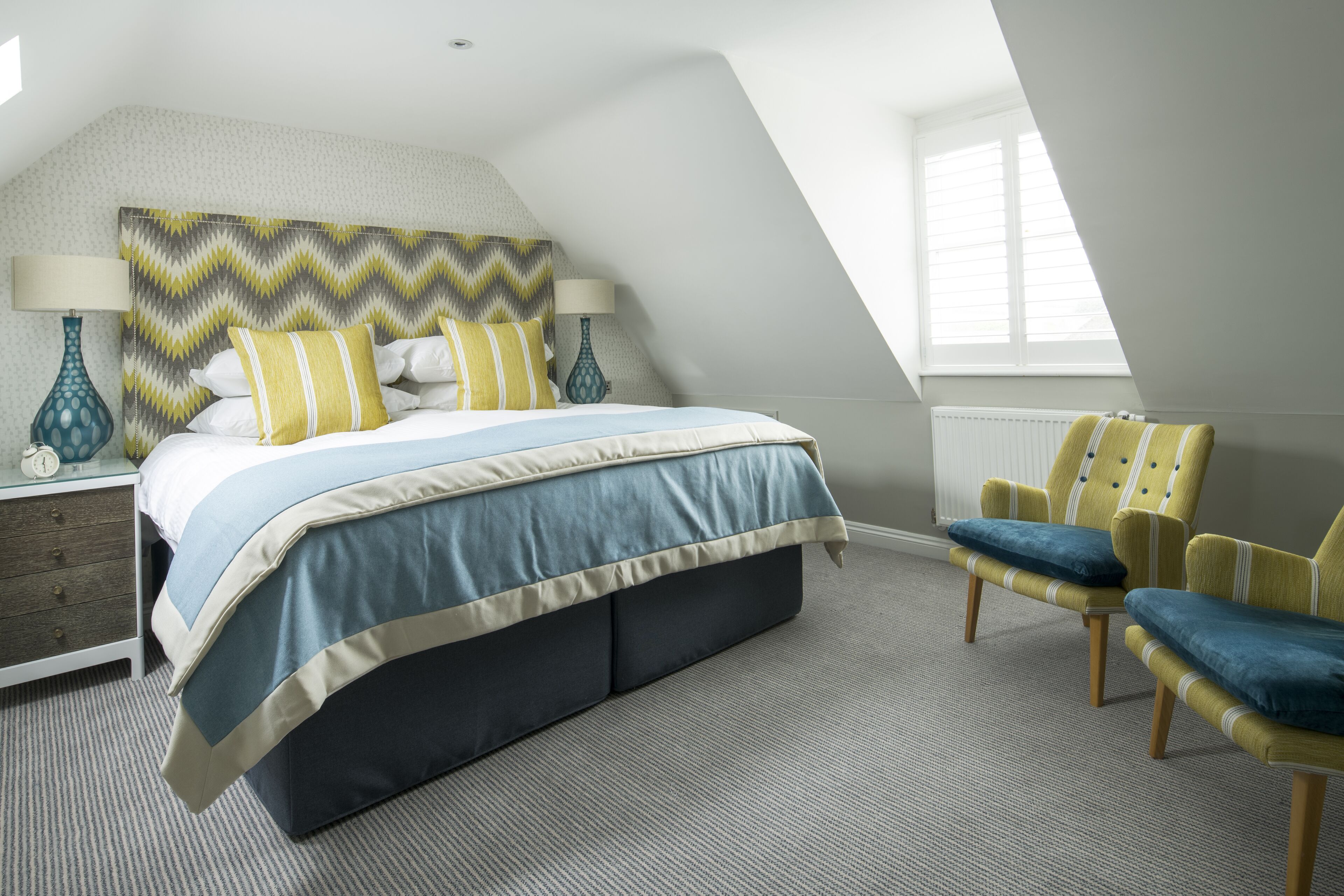 A bedroom with a bed, two chairs, a nightstand, and a lamp.