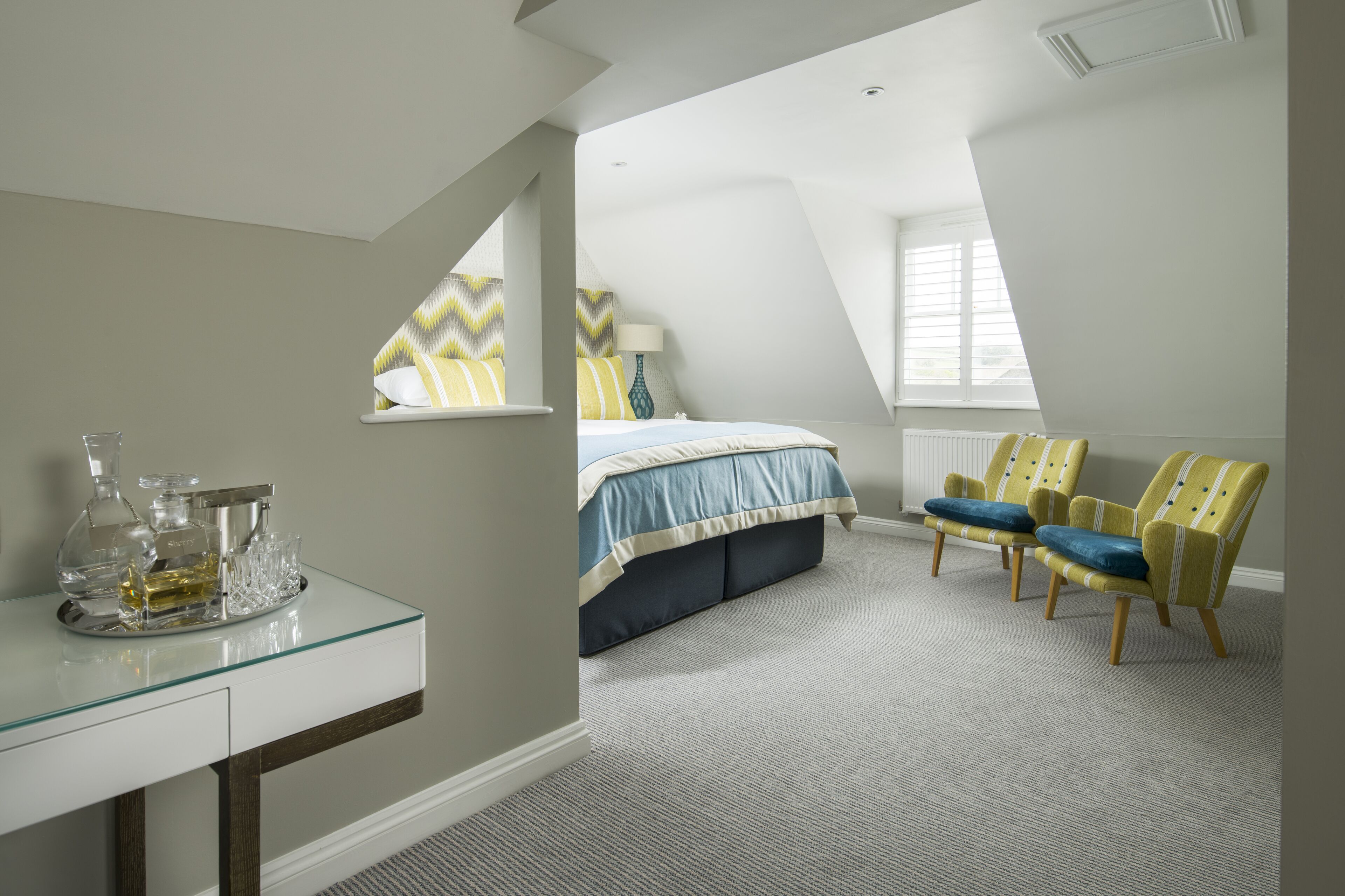 A bedroom with a bed, two chairs, a glass table with bottles, and a window.