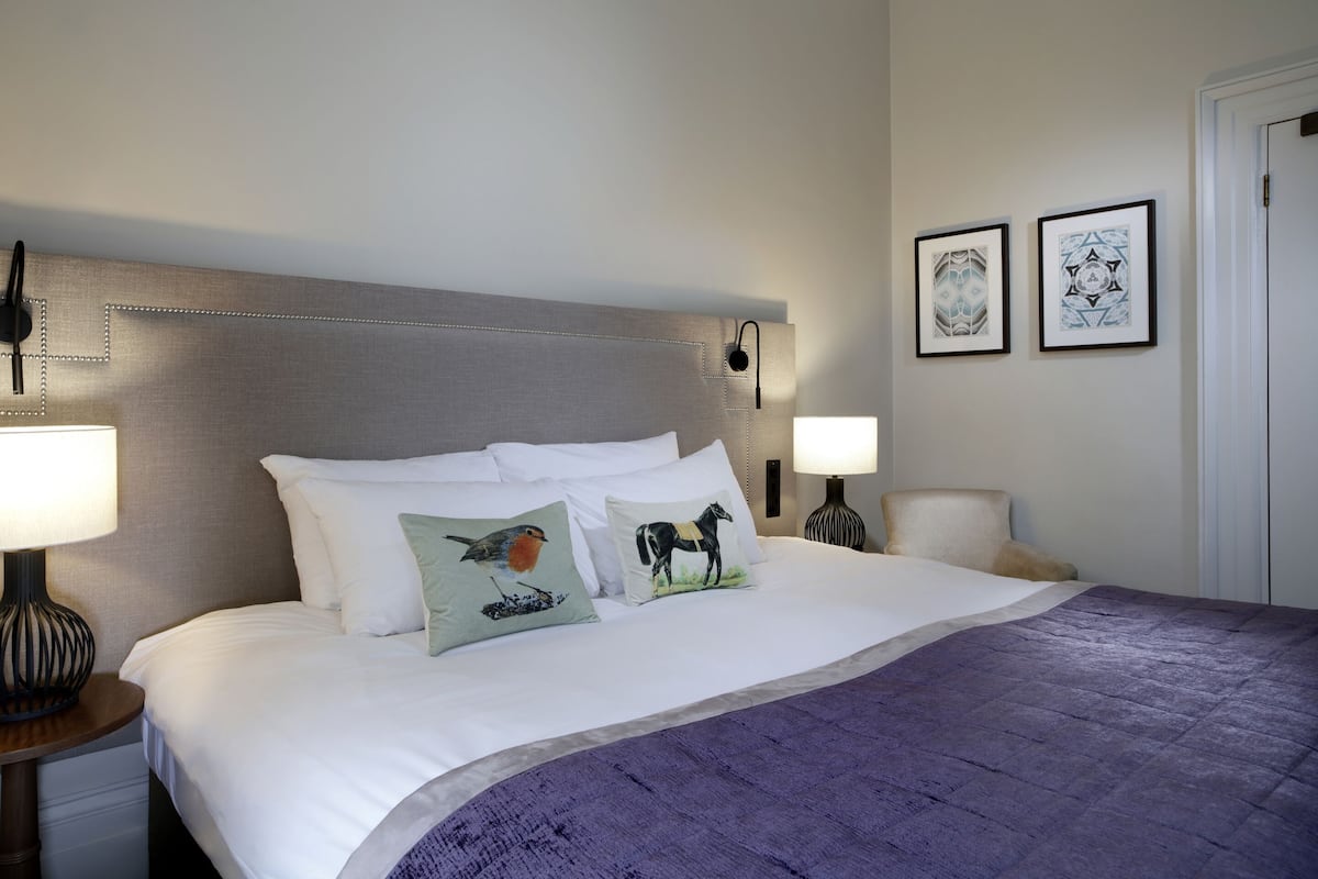 A neatly made bed with white linens and a purple throw blanket, flanked by two bedside lamps and a nightstand.