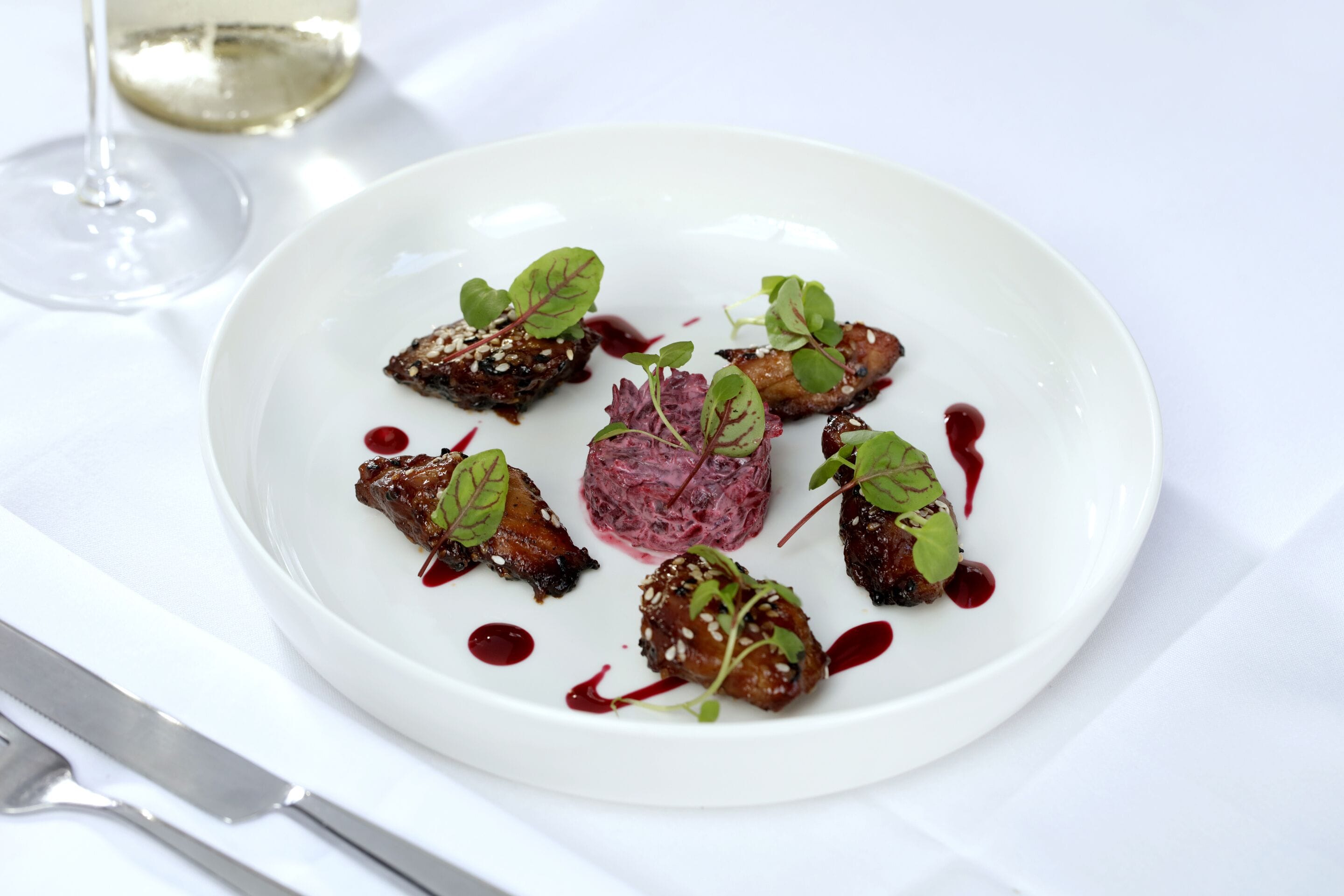 A white plate with food and a glass of white wine on a table.