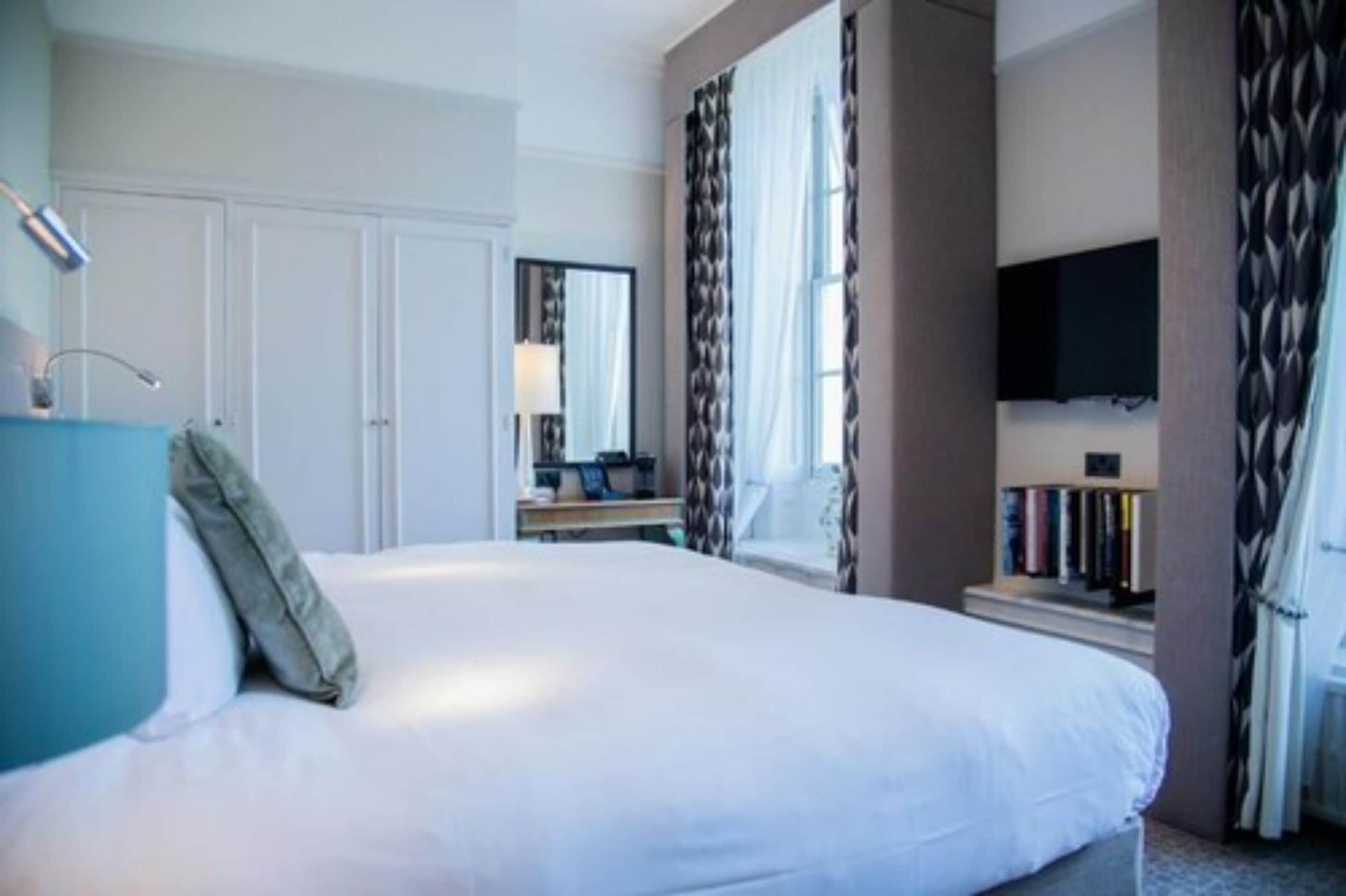 Een hotelkamer met een groot bed, een bureau met een computer, een aan de muur bevestigde televisie en een boekenplank.