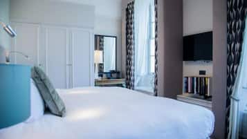 A hotel room with a large bed, a desk with a computer, a TV mounted on the wall, and a bookshelf.