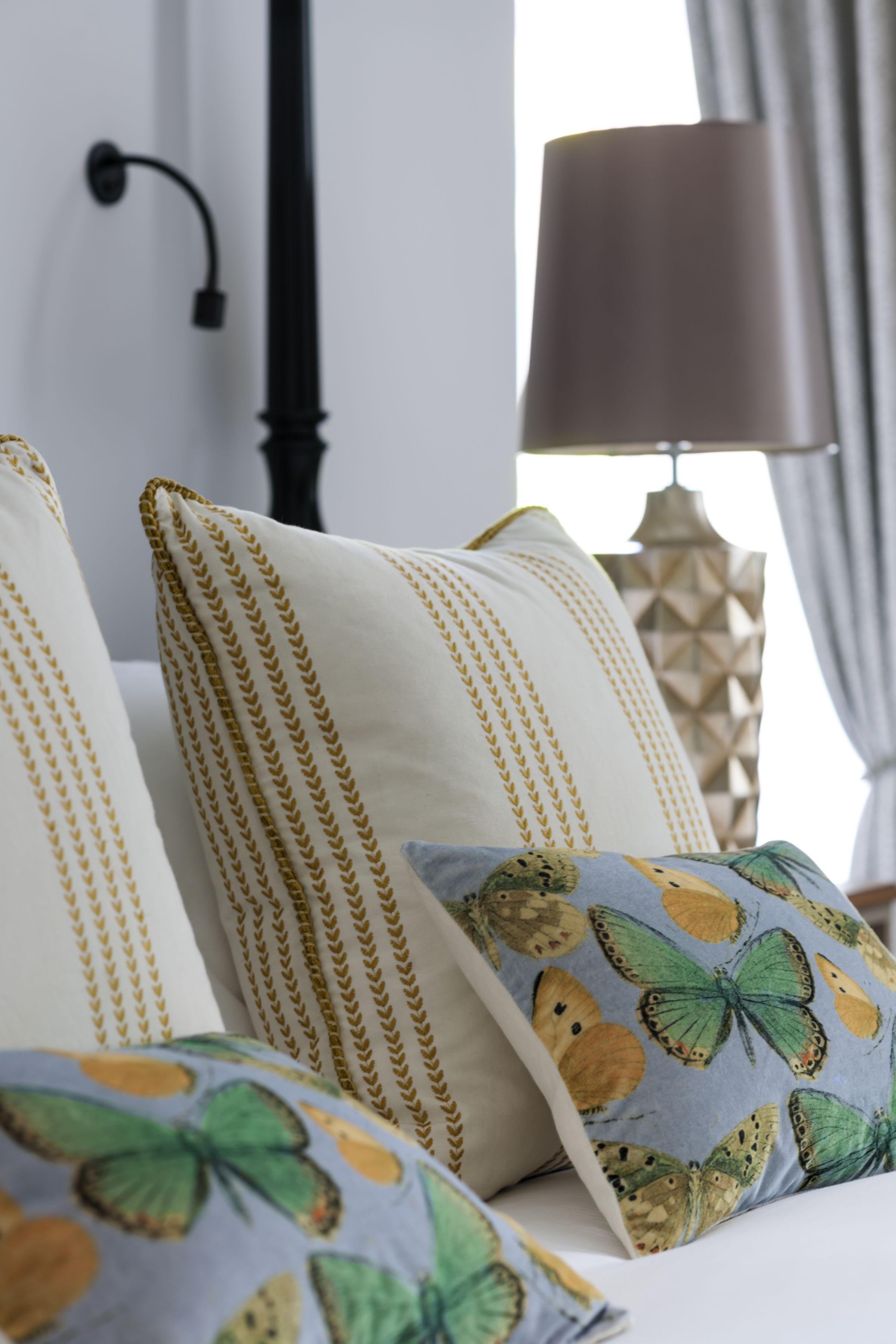 A bed with pillows featuring a butterfly pattern and a geometric lamp in the background.